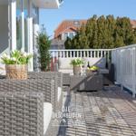 Terrasse mit Rattanmöbeln, Blumen und Blick auf Haus und Bäume.