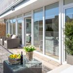 Terrasse mit Sitzgruppe, Tisch und Pflanzen. Große Glasfront zum Innenraum.