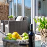 Terrasse mit Sitzgruppe, Blumen und Obst. Hintergrund: Glasfront und Holz-Zaun.