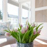 Tulpen in Vase auf Tisch vor Fenster mit Blick auf Balkon.