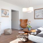 Wohnzimmer mit Sofa, Sessel, Tisch und Wandbildern.