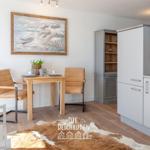 Essbereich mit Tisch, zwei Stühlen und Küchenzeile. Wandbild zeigt Strandmotiv.