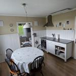 Küche mit Esstisch, Herd und Fenster. Weiße Schränke und Holzboden.