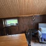 Raum mit Holzwand, Sitzgelegenheit und Tisch. Fenster mit Schild BEACH.