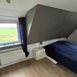 Schlafzimmer mit Dachschrägen, Bett, Fenster und Blick auf Feld.