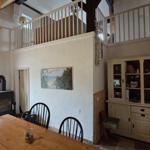 Essbereich mit Holztisch, schwarzen Stühlen und Kaminofen. Obergeschoss mit Balkon.