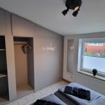 Schlafzimmer mit Kleiderschrank, Bett und Fenster mit Blick auf Außenbereich.