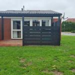 Einfamilienhaus mit Garten, Garage und Terrasse. Modernes Design mit rotem Backstein und schwarzem Zaun.