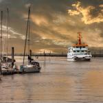Hafen mit Segelyachten und einem weißen Schiff im Sonnenuntergang.