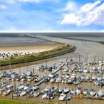 Hafen mit vielen Booten, Strand und Wattgebiet unter blauem Himmel.