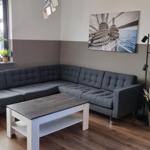 Ein Wohnzimmer mit grauem Ecksofa, Holzfußboden und Wandbild mit Seil.