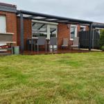 Terrasse mit Tisch, Stühlen und Sitzgelegenheiten. Grasfläche und Grillbereich vor Haus.