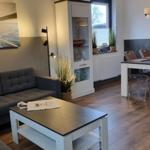 Wohn- und Essbereich mit Sofa, Tisch und Stühlen. Wandbild mit Seil und Meer.