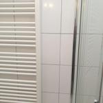 Shower area with glass door and heater against white tiled wall
