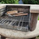 Stone barbecue with grill grate and spatula in the garden.