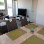 Dining area with table and chairs, TV and sofa in background.