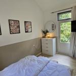 Schlafzimmer mit Bett, Schrank, Fernseher und Fenster zur grünen Außenseite.