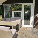 Terrasse mit Sitzgruppe und Tisch. Holzwand und Glastür zum Innenraum.