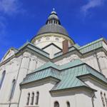 Weißes Kirchengebäude mit kupferfarbenem Dach und Kuppel unter blauem Himmel.