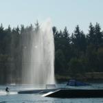 Wasserskifahrer beim Springen über Sprungbrett und Fontäne am See.