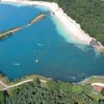 Aerielansicht eines Sees mit Strand, Booten und Waldumgebung.