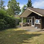 Holzhaus mit Terrasse, Garten und Satellitenanlage. Gartenmöbel und Fenster sichtbar.