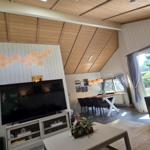 Wohn- und Essbereich mit TV, Sofa und großem Fenster. Holzdecke und weiße Wände.