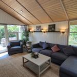 Wohnzimmer mit Sofa, Sessel und Tisch. Holzdecke und Fenster zur Außenterrasse.
