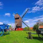 Holzwindmühle mit blauem und grünem Wagen auf grünem Rasen.