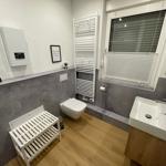 Badezimmer mit Toilette, Waschbecken und Heizung. Holzboden und Fenster mit Jalousie.