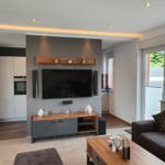 Wohnzimmer mit TV, Sofa und Küchenbereich im Hintergrund.