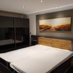 Schlafzimmer mit Doppelbett, Kleiderschrank und Wandbild.