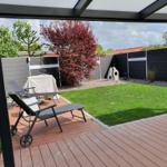 Terrasse mit Liegestühlen und Grünfläche hinter Schutzwand.