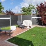 Hinterhof mit Terrasse, Liegestühlen und Rasenfläche.