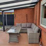 Terrasse mit Sitzgruppe, Glas-Tisch und Dachüberdachung an roter Ziegelwand.