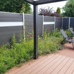 Terrasse mit Liegestühlen und Blumenbeet an grauer Holzumzäunung.