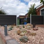 Hinterhof mit Steinbeete, dunklem Zaun und Terrasse. Mehrere Mülltonnen sind sichtbar.