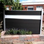 Moderne schwarze und weiße Sichtschutzwand vor einem Backsteinhaus mit Beet und Steinmauer.