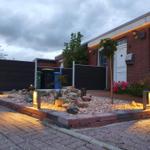 Haus mit gepflastertem Hof, Beleuchtung und Steinbeete. Eingangstür und Fenster sichtbar.