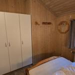 Schlafzimmer mit Holzwand, Bett, Kleiderschrank und Fenster mit Blick in den Wald.