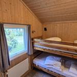 Zimmer mit Holzwand und Doppelstockbett. Fenster mit Vorhang und Heizkörper.