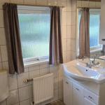 Badezimmer mit Waschbecken, Spiegel, Toilette und Fenster mit Vorhängen.