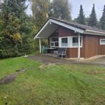 Holzhaus mit Terrasse, Garten und Bäumen im Hintergrund.