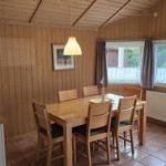 Essbereich mit Holztisch, sechs Stühlen und Fenstern mit Blick nach draußen.