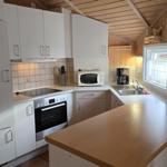 Küche mit weißen Schränken, Herd und Spüle. Holzwände und Dach.