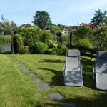 Zwei Liegestühle stehen auf einer grünen Wiese neben einem Gartenzaun und blühenden Rosen.