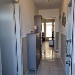 Flur mit Schrank, Tür und Wanddekoration. Blick in Wohnbereich mit Fenster.