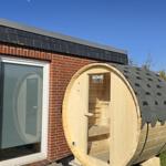 Holzsauna mit Dach und Sitzbänken an einer Backsteinmauer.