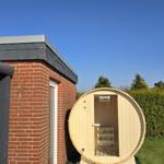 Außenliegende Holzsauna neben einem Backsteinhaus mit grünem Rasen und Hecken.