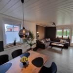 Wohn- und Essbereich mit Sofa, Tisch und Pflanzen. Holzboden und große Fenster.